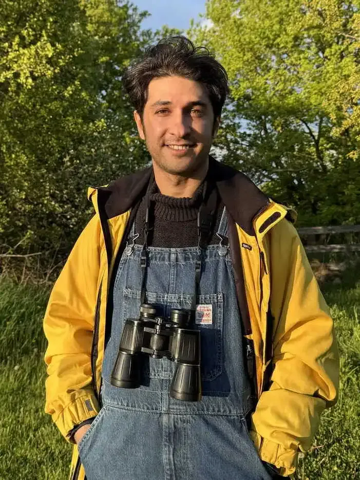 Masoud Ahmadi standing on the Willoway property in work overalls with binoculars around his neck, trees behind him.